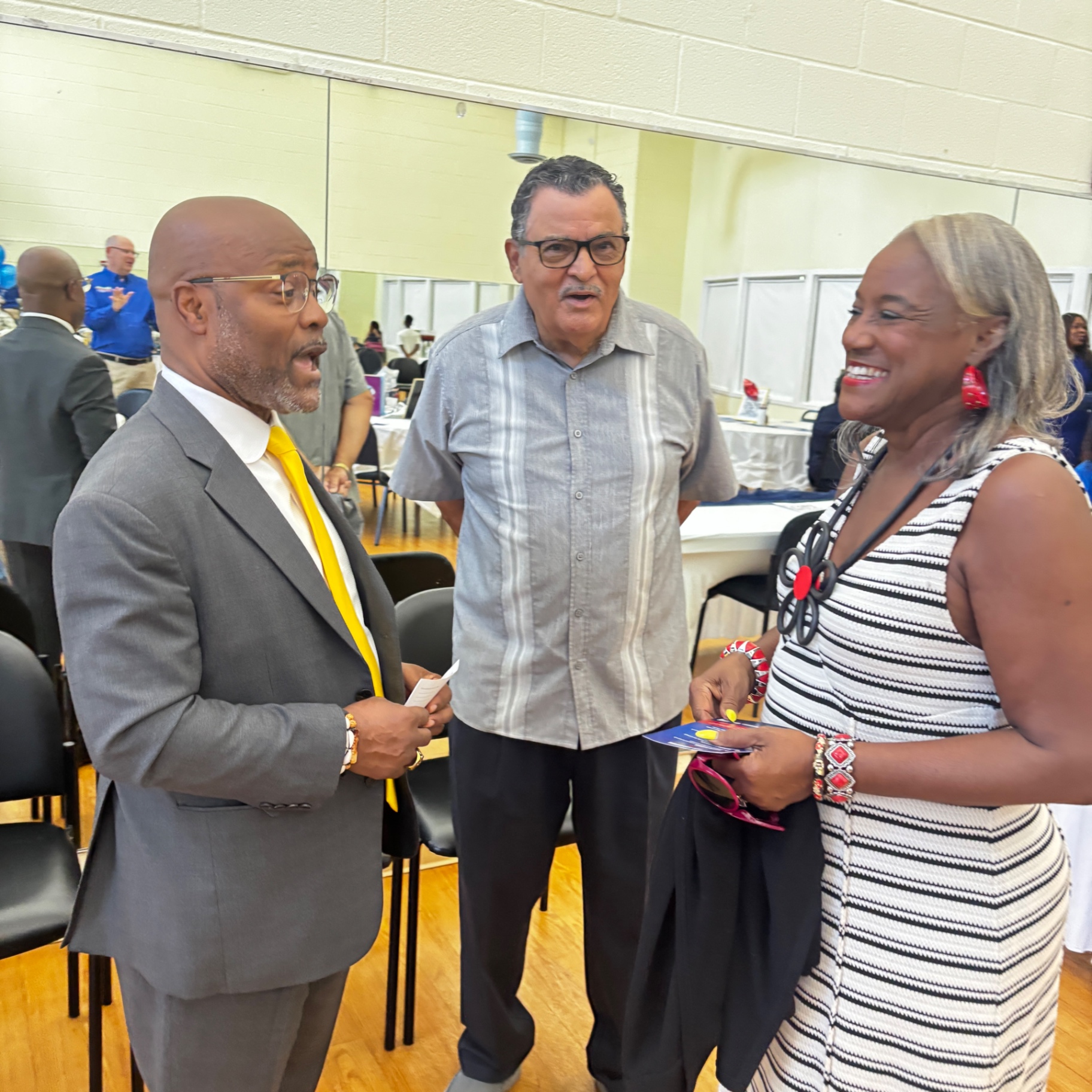 Jason Samuels in a grey suit and yellow tie talks with attendees at the August 23 kickoff event.